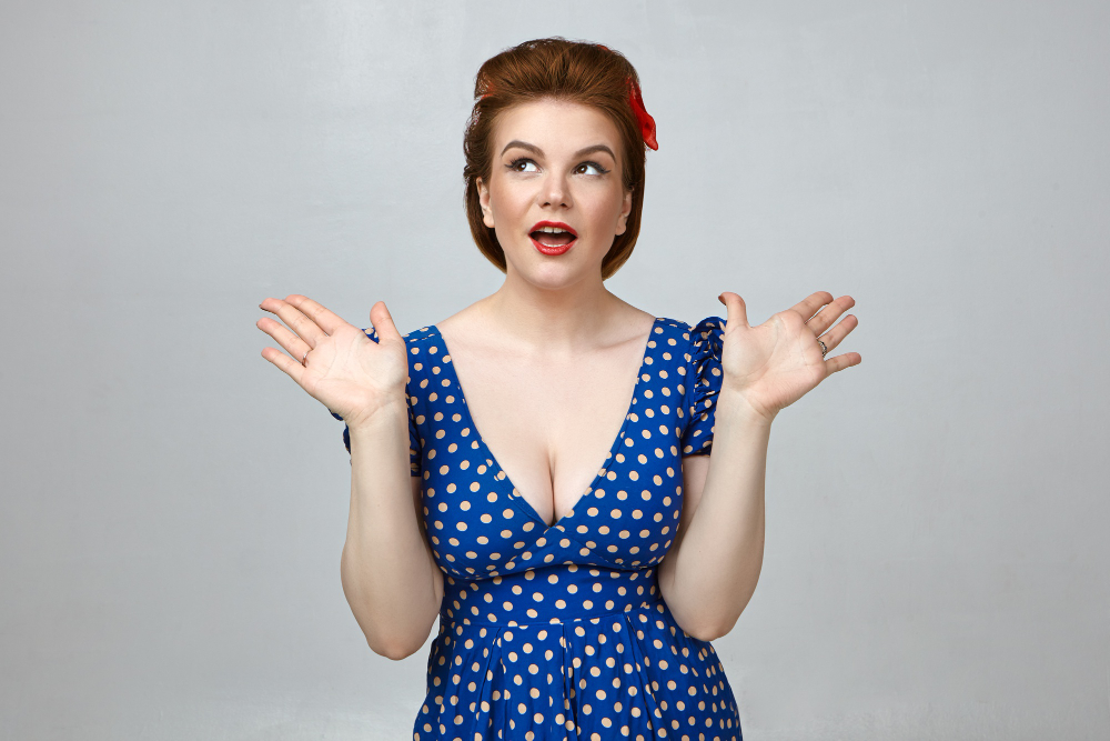 studio shot of attractive gorgeous young woman wearing stylish retro dress with low cut and red lipstick gesturing emotionally exclaiming in